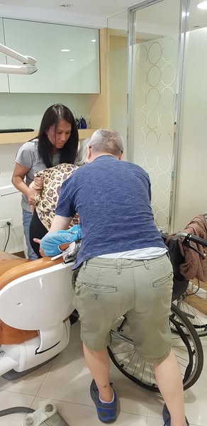 兒子悉心將母親抱上診療椅