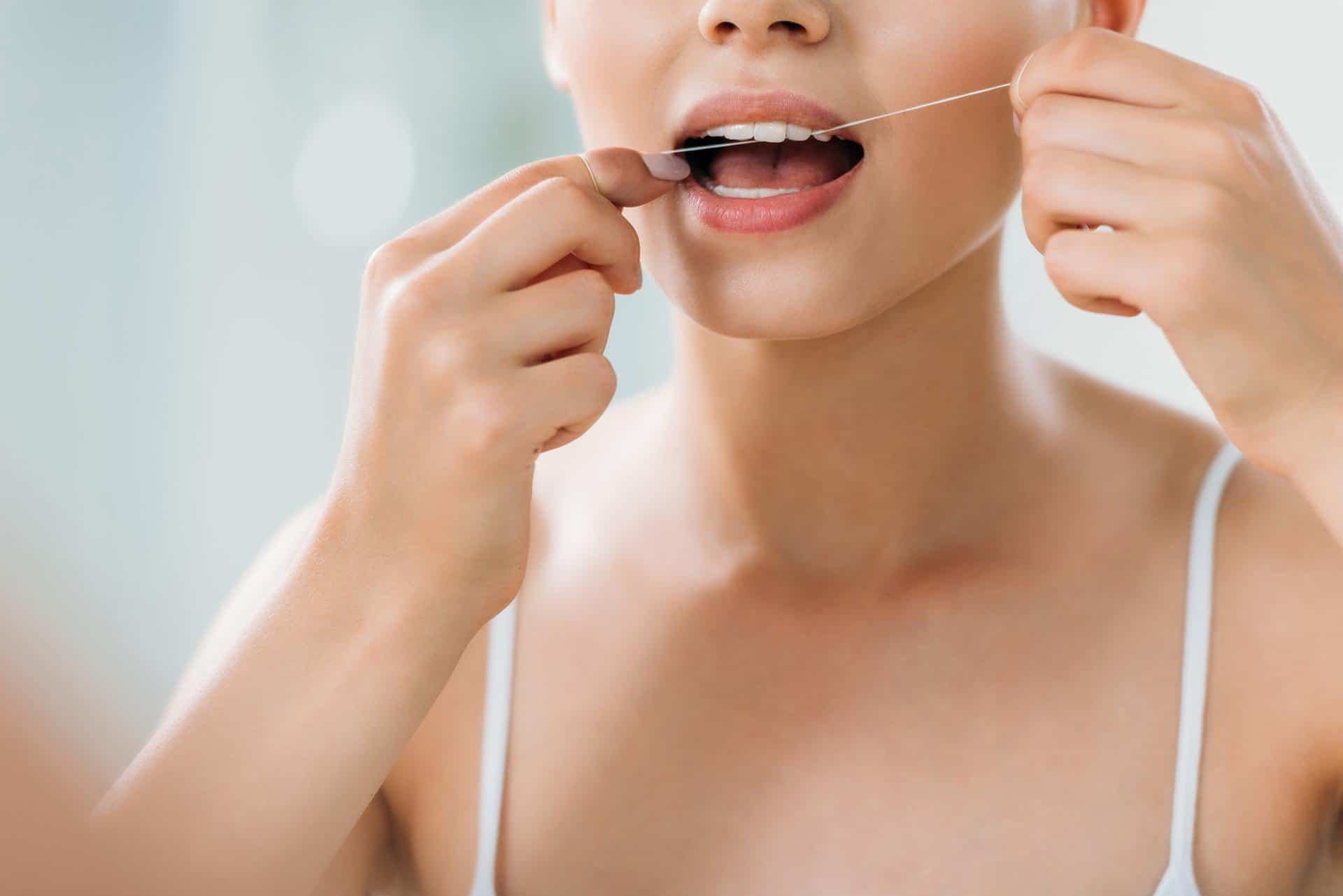 cropped shot of young woman using dental floss in bathroom